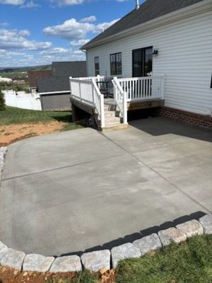 Newly poured concrete patio next to a white house with a deck. The patio has a stone border.