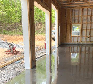 Newly poured concrete floor inside a partially constructed garage with exposed wooden beams and framing.