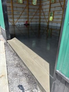 Newly poured concrete floor in a building under construction, with a visible threshold and a partially constructed wooden frame.