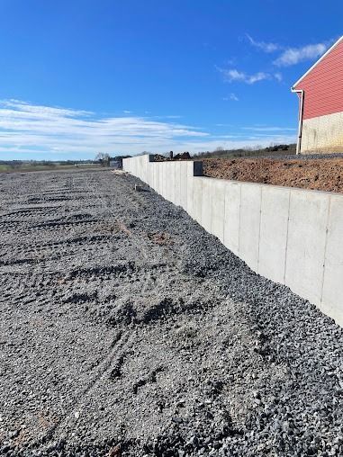 A concrete retaining wall with gravel base next to a construction site under a blue sky.