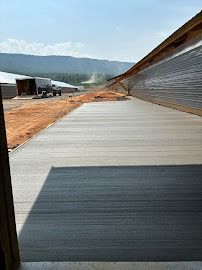 A newly poured concrete surface leads away from a building, with a truck and mountains in the background.