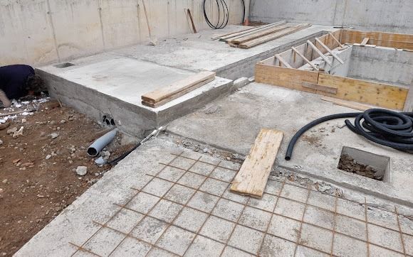 Construction site with concrete forms, rebar grid, piping, and wooden planks.