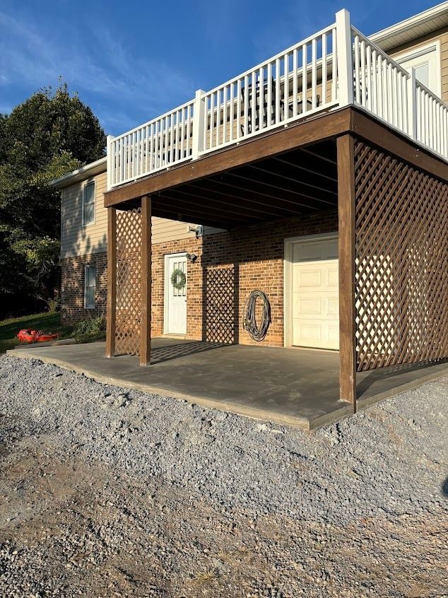Two-story house with a brown latticed carport, garage, and a deck with white railings. Gravel ground.