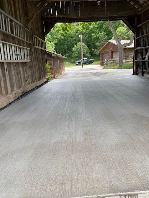 Inside of a wooden barn, looking out at a paved road, a vehicle is parked.