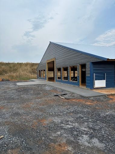 Building with blue siding and a dark roof under construction on a gravel lot.