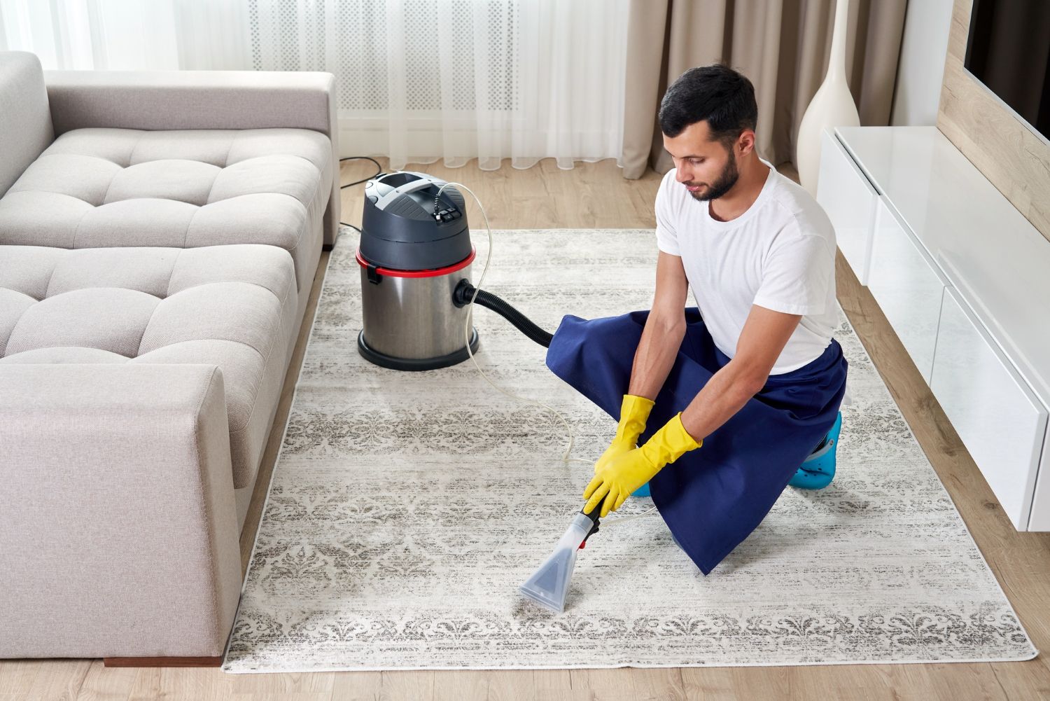 A man is cleaning a rug in a living room with a vacuum cleaner.
