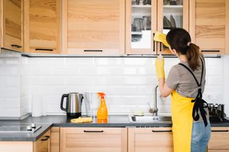 a woman in a yellow apron is cleaning the cabinets in a kitchen