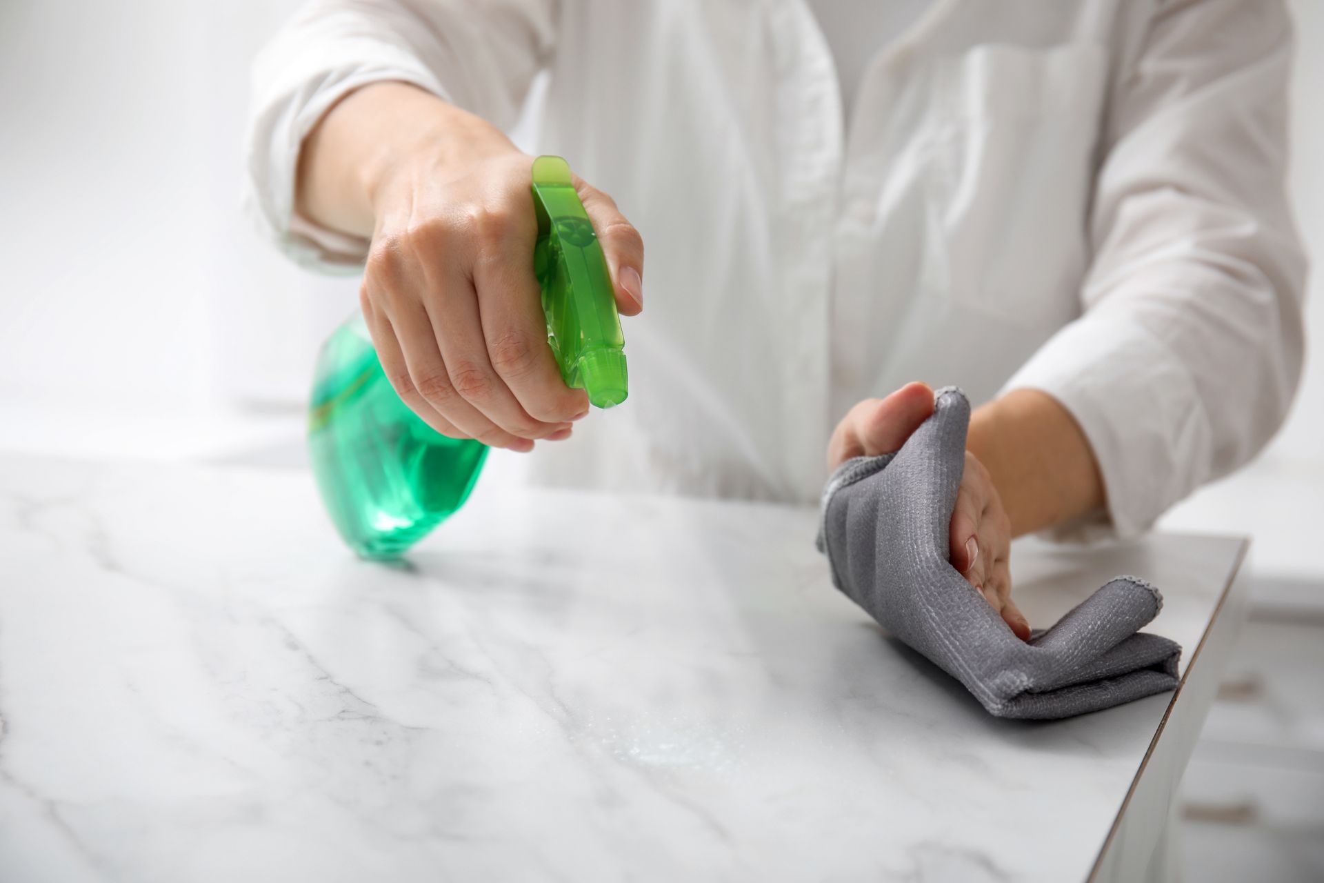 A woman is cleaning a marble counter top with a cloth and spray bottle.