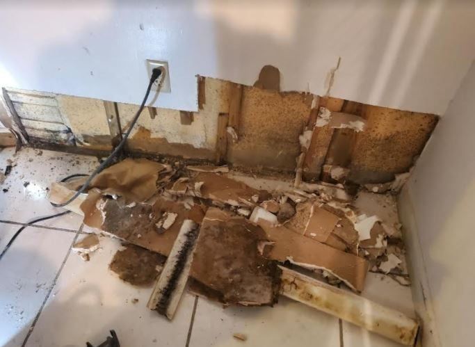 A room with a hole in the wall and a lot of pieces of paper on the floor.