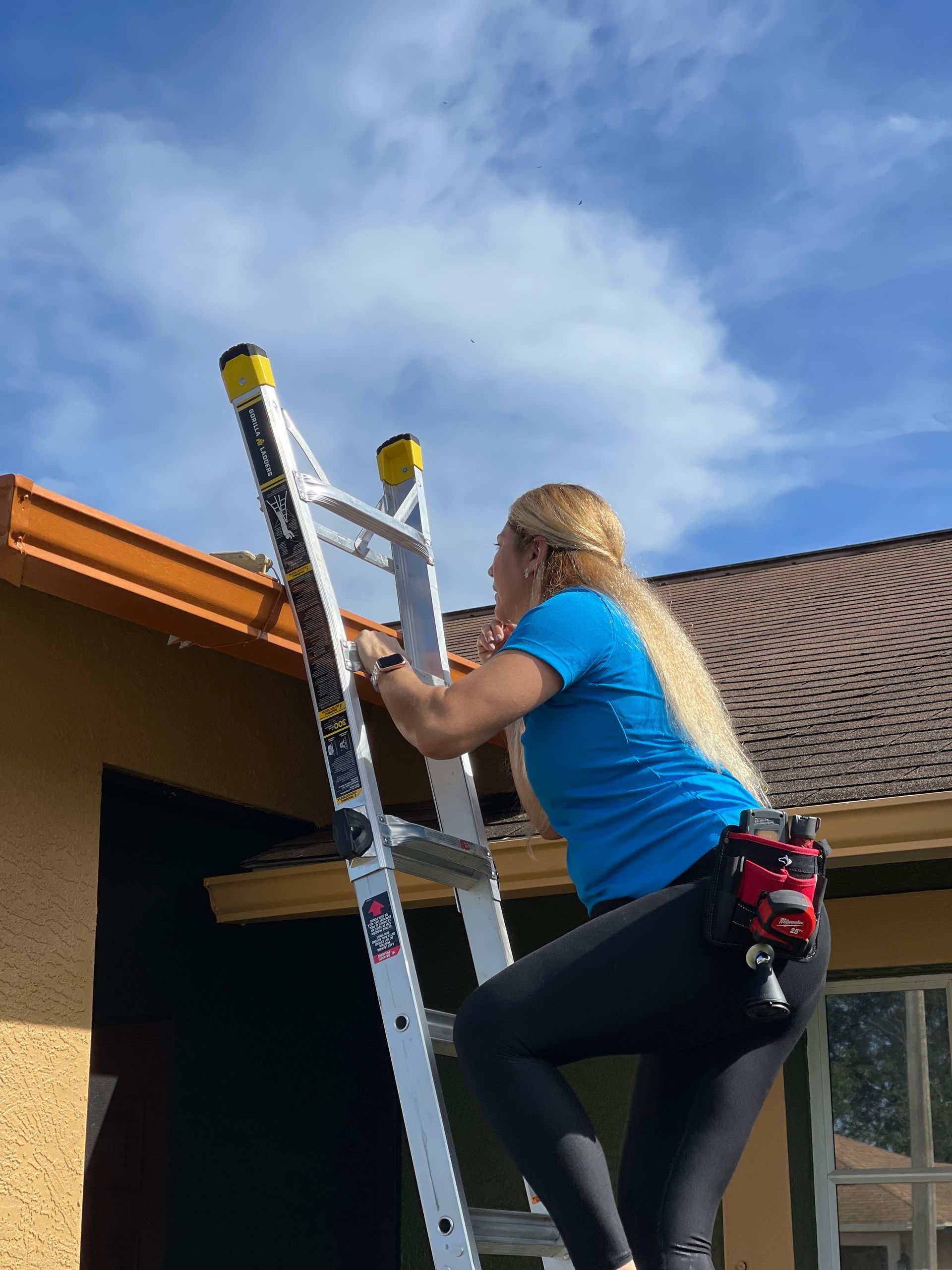 A woman is climbing a ladder to fix a gutter on a house.