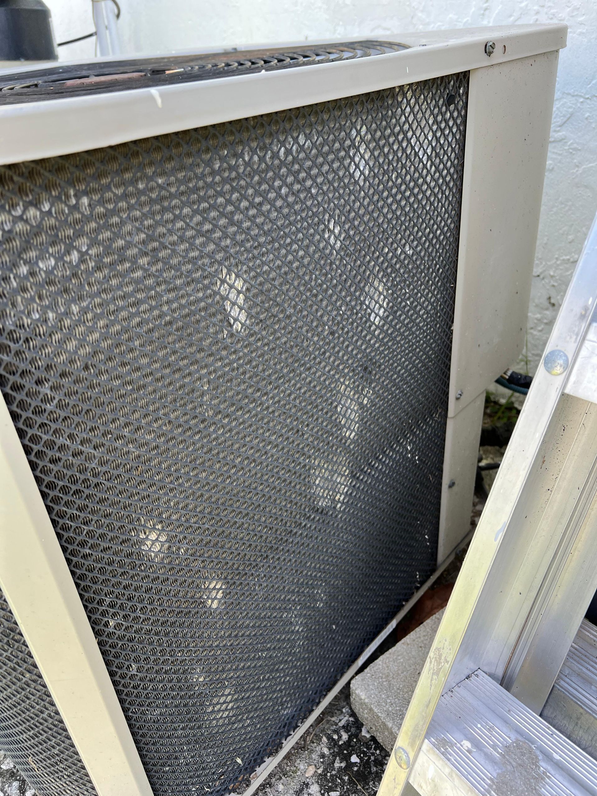 A close up of a dirty air conditioner with a ladder in the background.