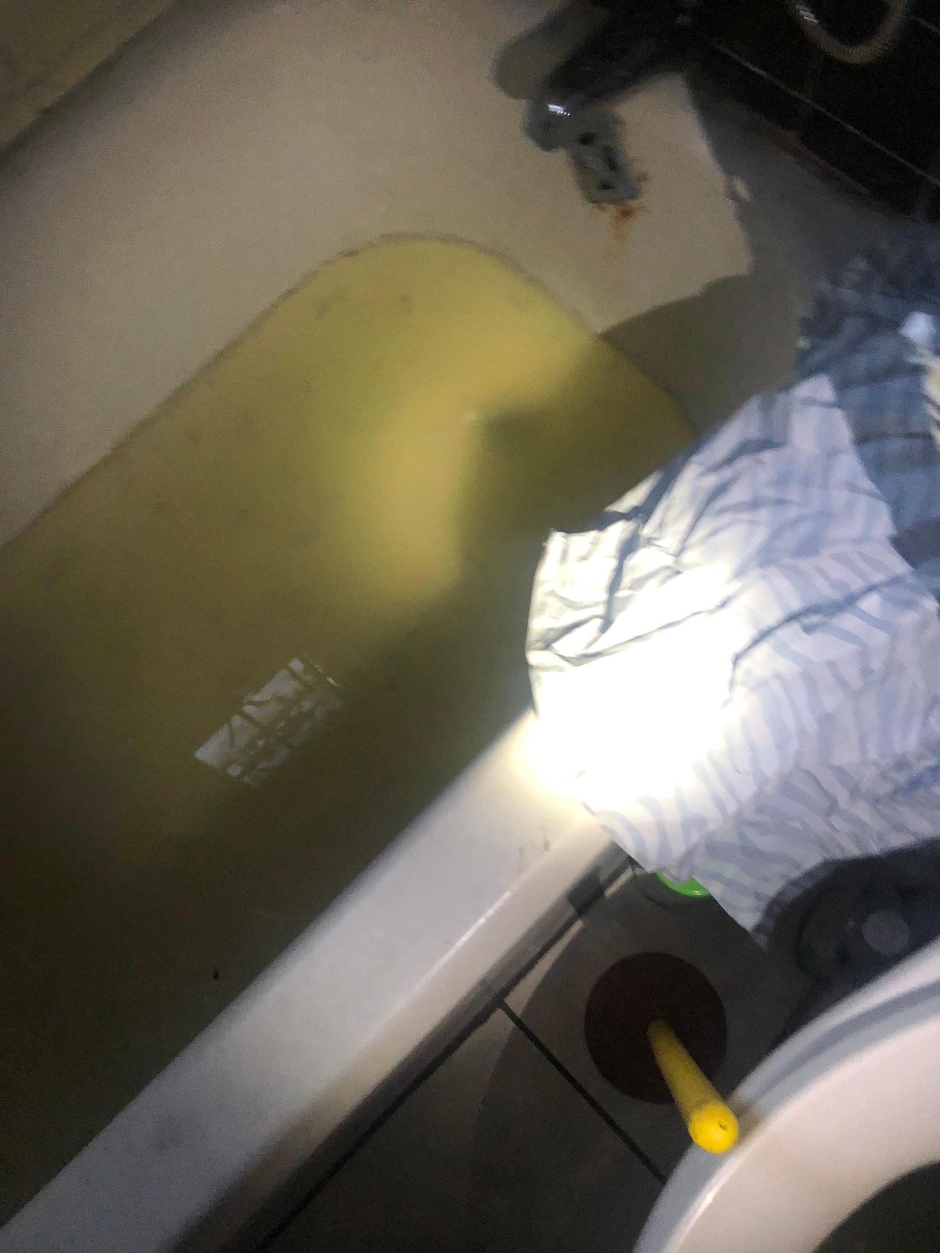 A bathtub filled with yellow water next to a toilet.