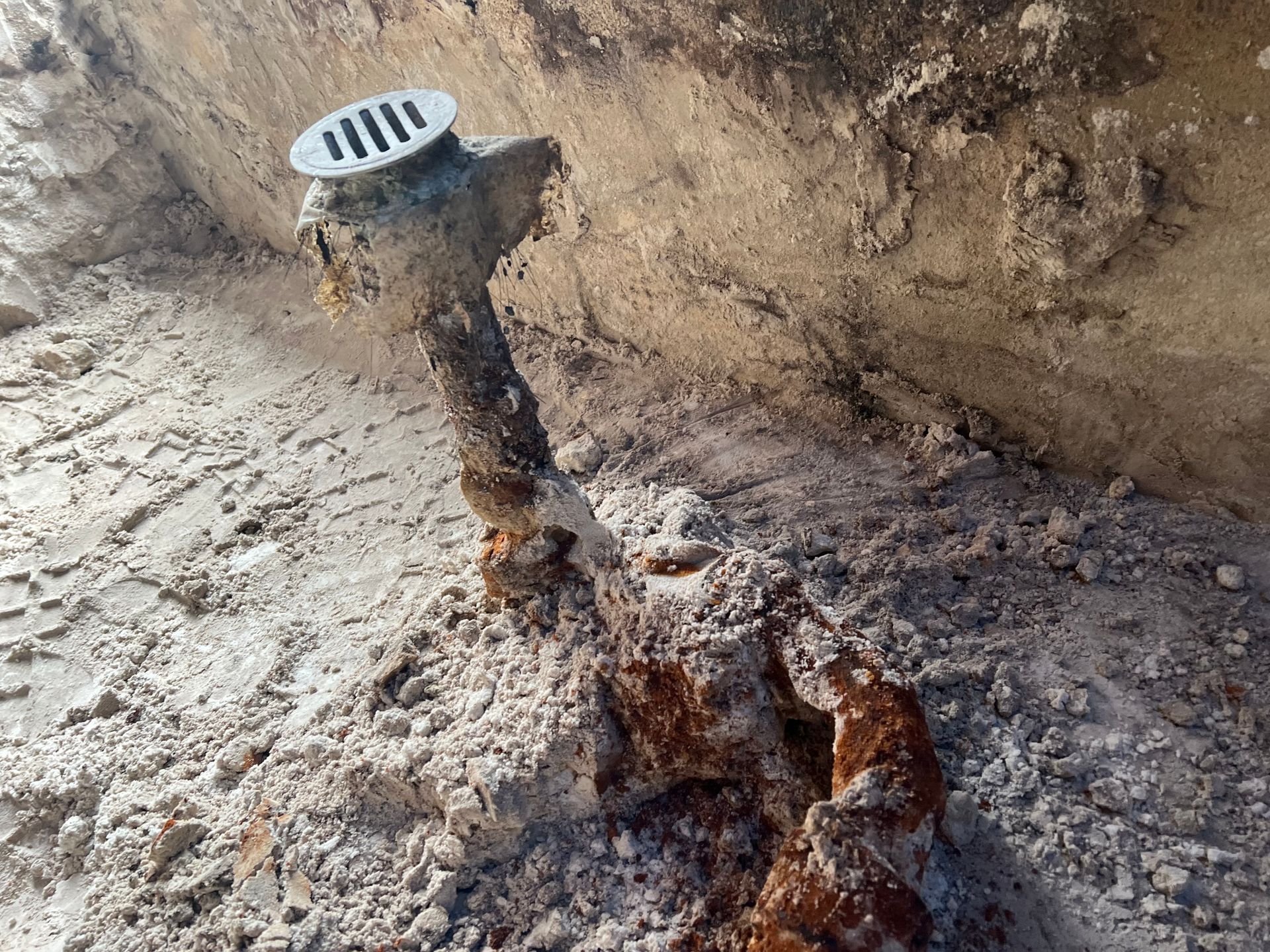 A rusty pipe is sitting in the dirt next to a wall.