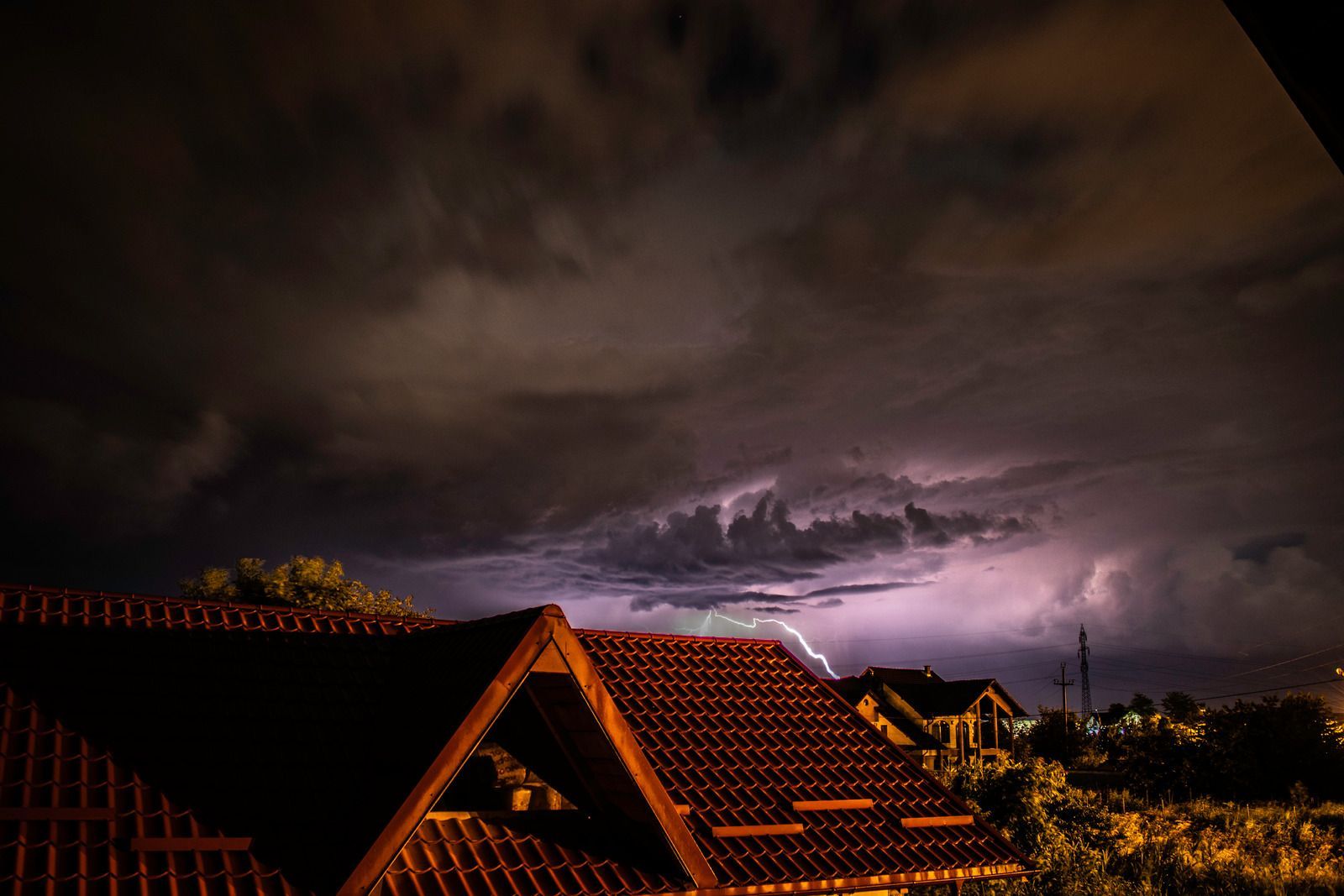 A lightning storm is coming over a roof of a house at night.