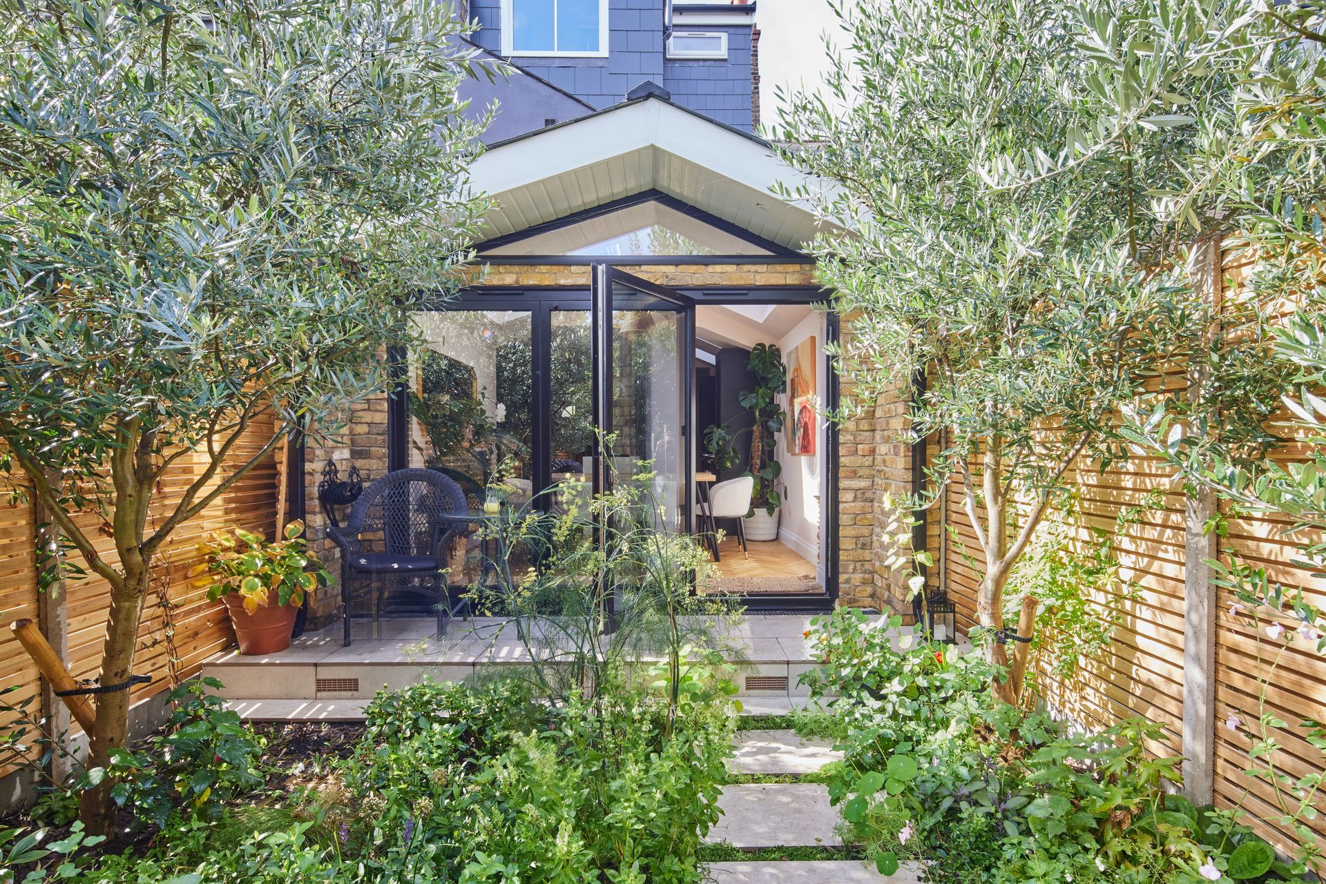 The back of a house with a patio and trees in front of it.
