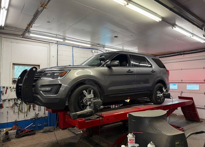 A gray police SUV on a red car lift in a repair shop, undergoing wheel alignment. | Easton Auto Body