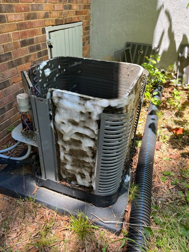 Outdoor HVAC unit with frosty coils beside a brick wall and grass-covered ground