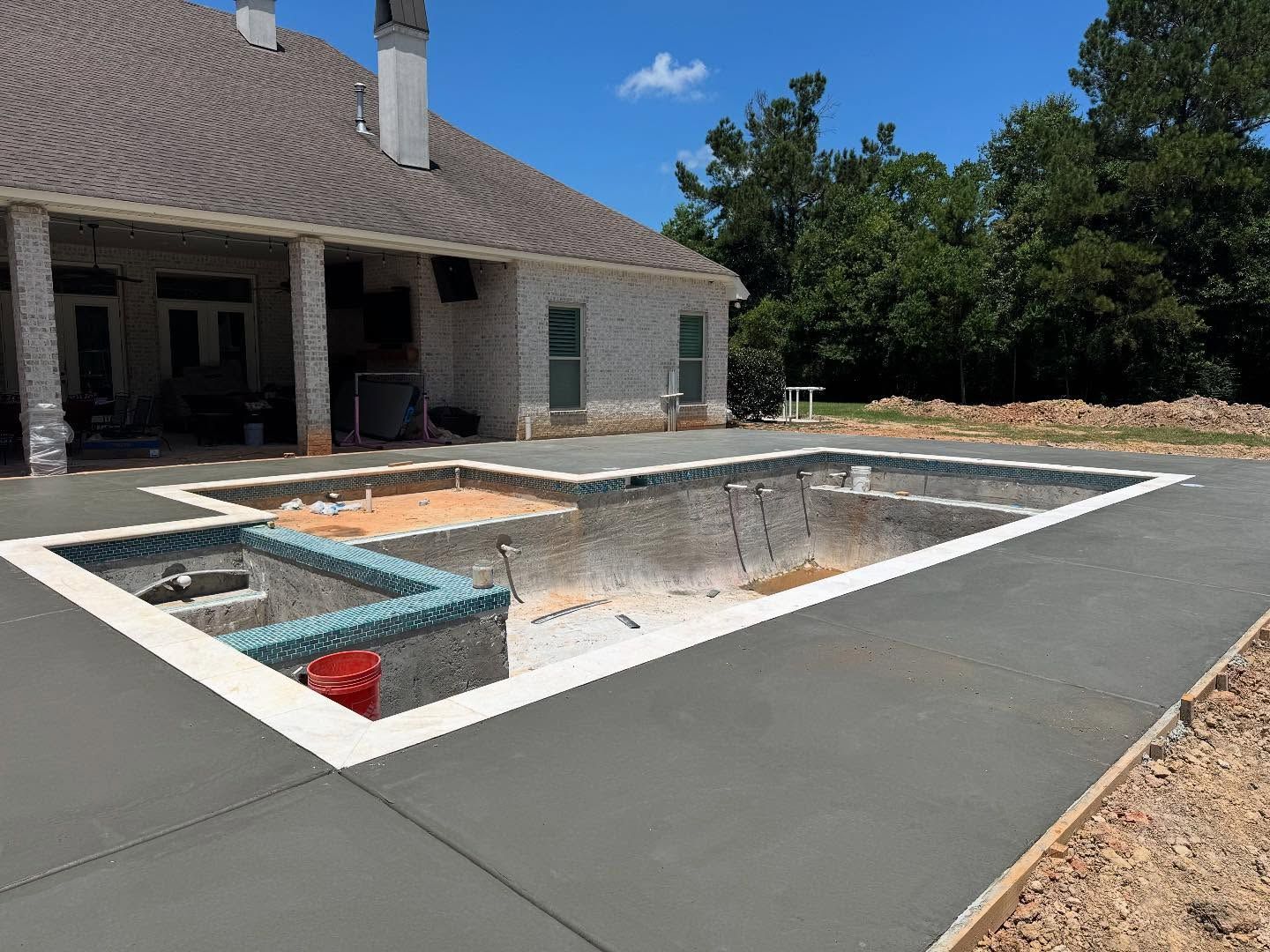 A rectangular swimming pool under construction next to a house. Concrete surrounds the pool; the pool is empty.