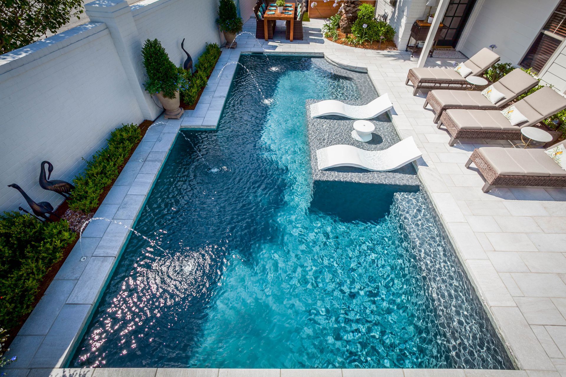 A modern, rectangular pool with blue water, surrounded by white stone and lounge chairs.