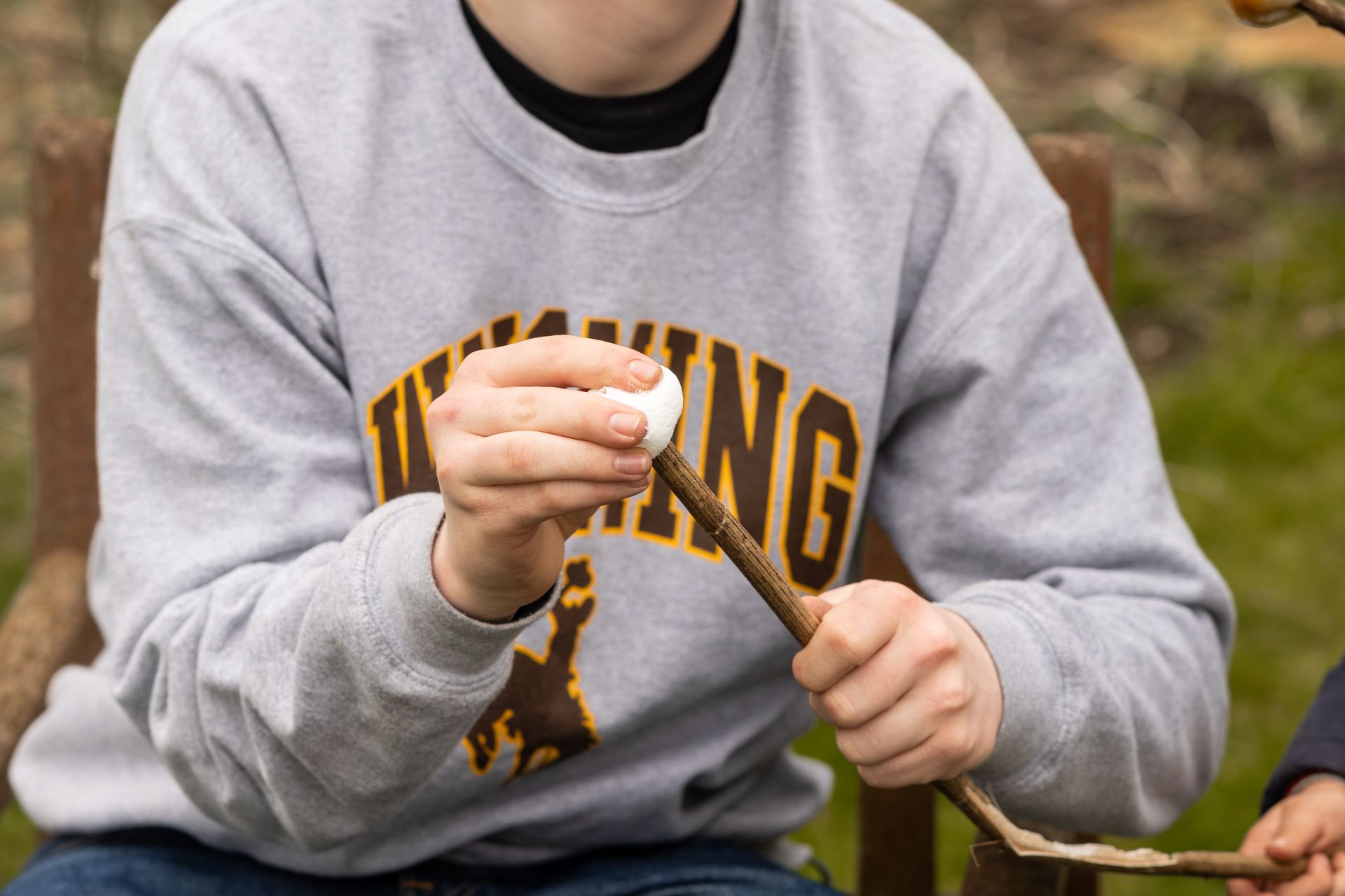 A person wearing a vikings sweatshirt is holding a stick and a marshmallow.