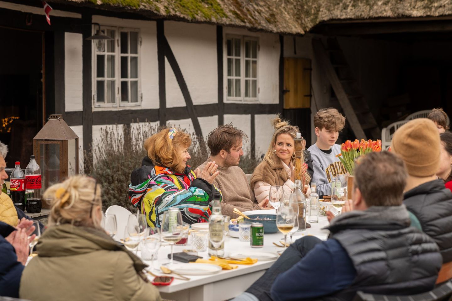 A group of people are sitting at a table in front of a thatched building.