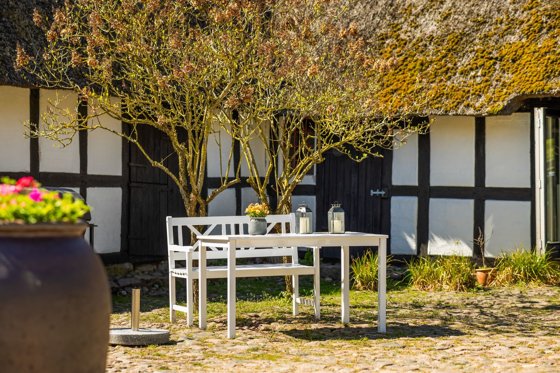 A table and bench are in front of a thatched roof house.