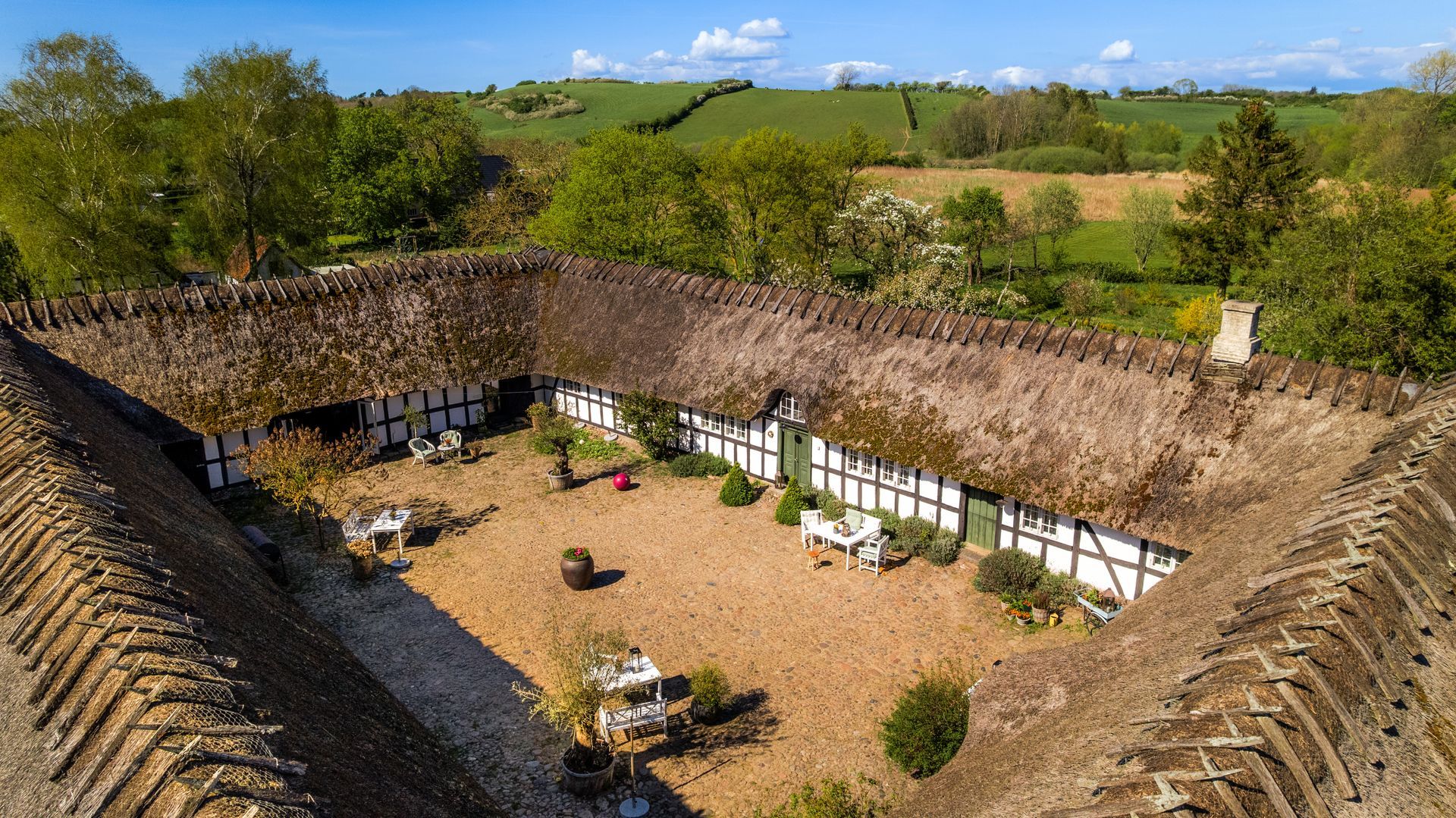 An aerial view of a thatched roofed house in the countryside.