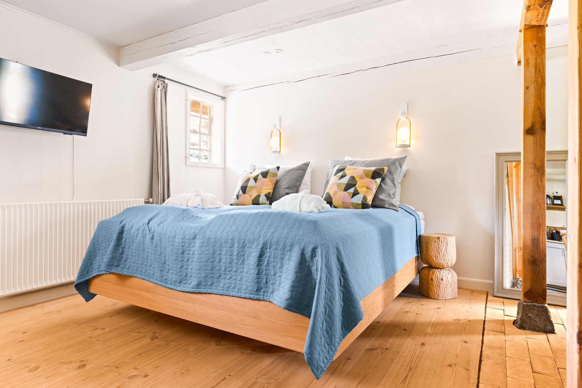 A bedroom with a large bed , dresser , bench , and television.