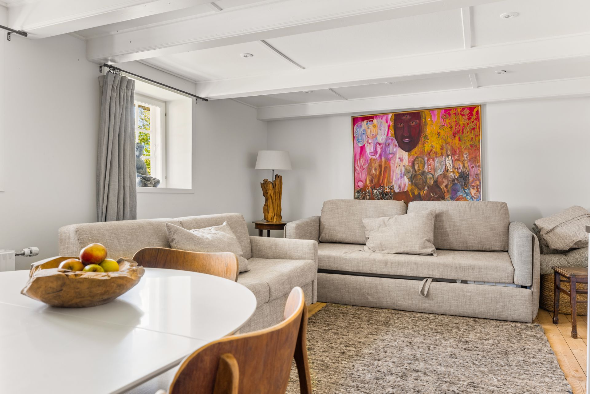 A living room with a couch , table , chairs and a painting on the wall.