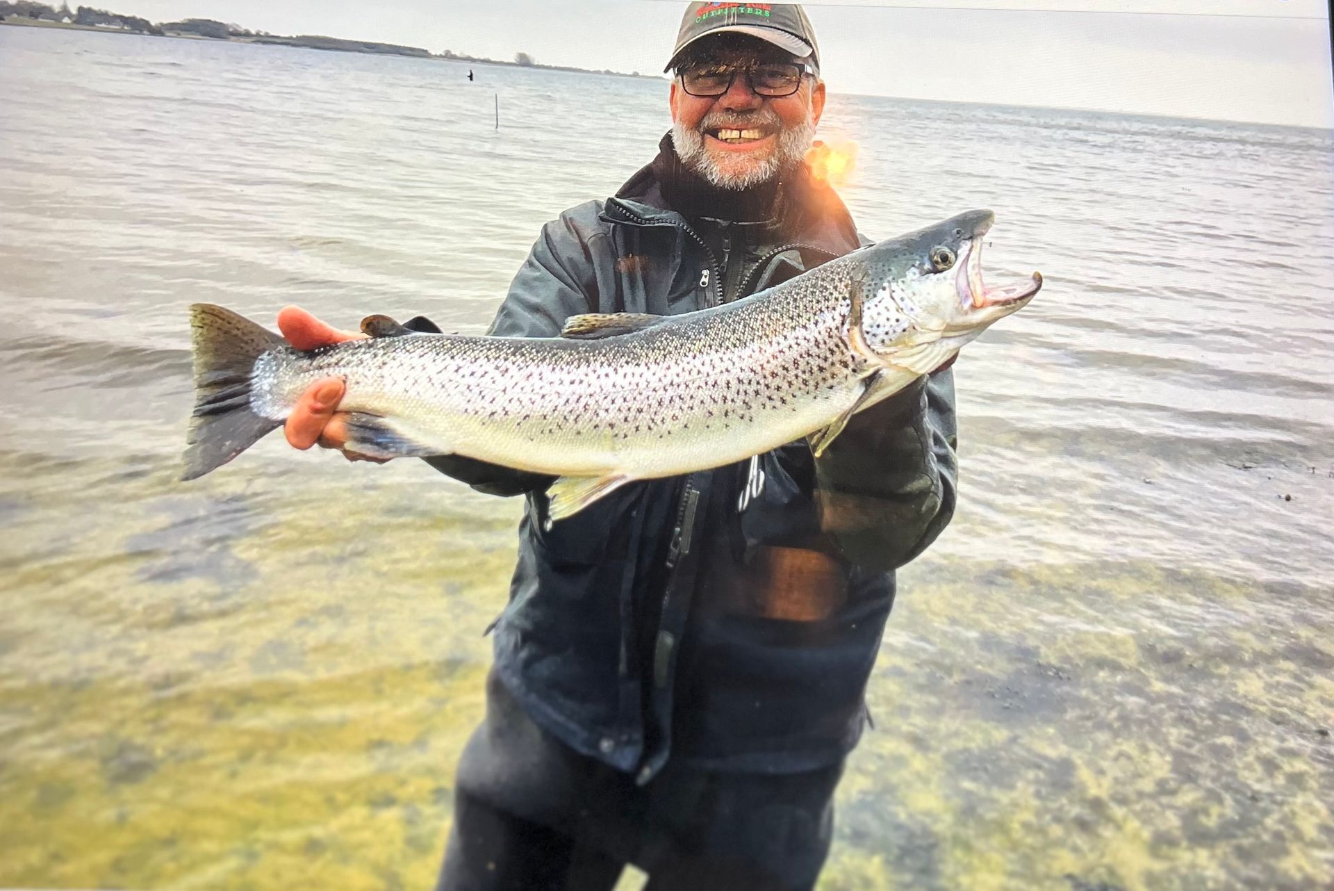 Beaming angler standing in the sea, proudly holding a large silver trout. Incredible fishing trips and experiences