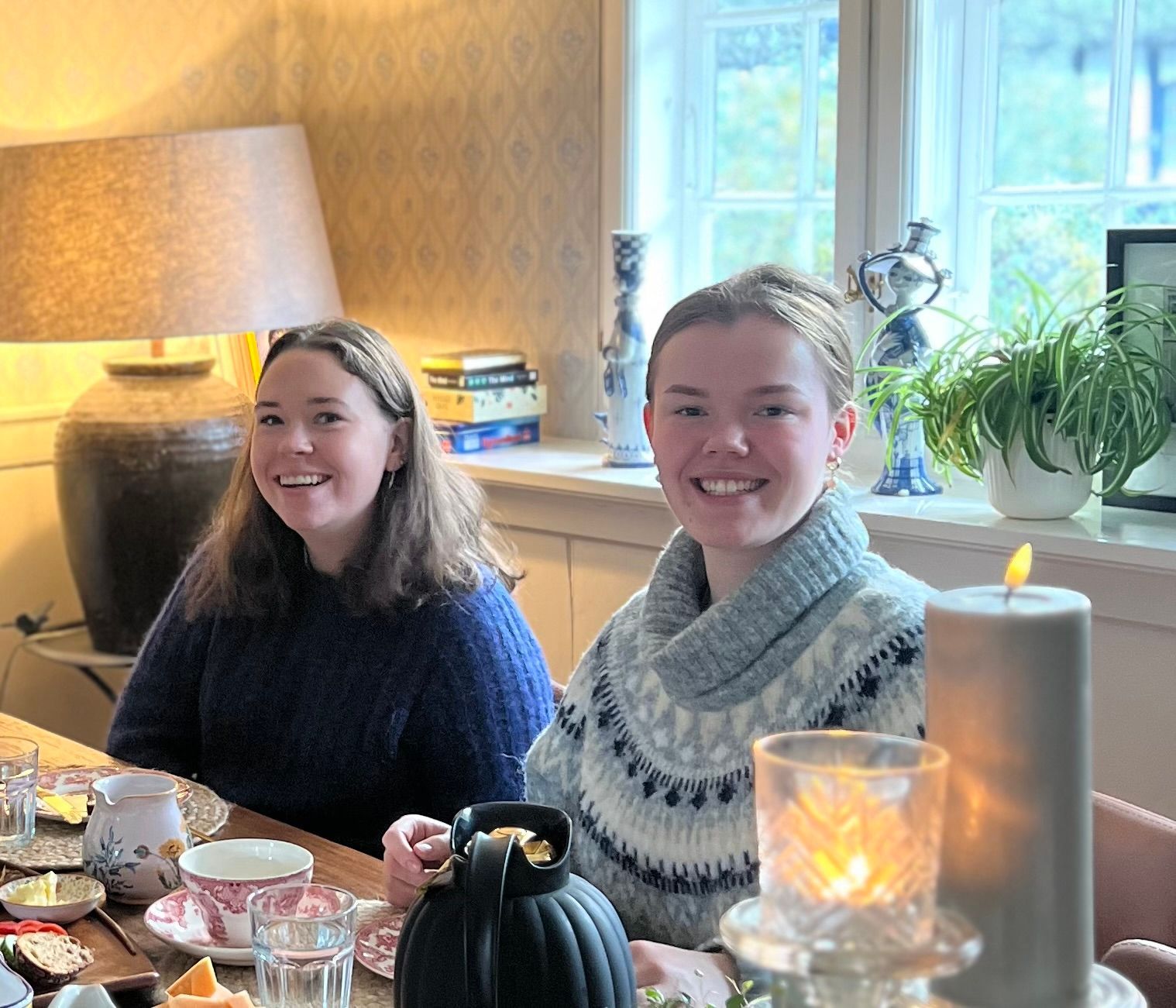 Two women are sitting at a table with a pumpkin and candles.