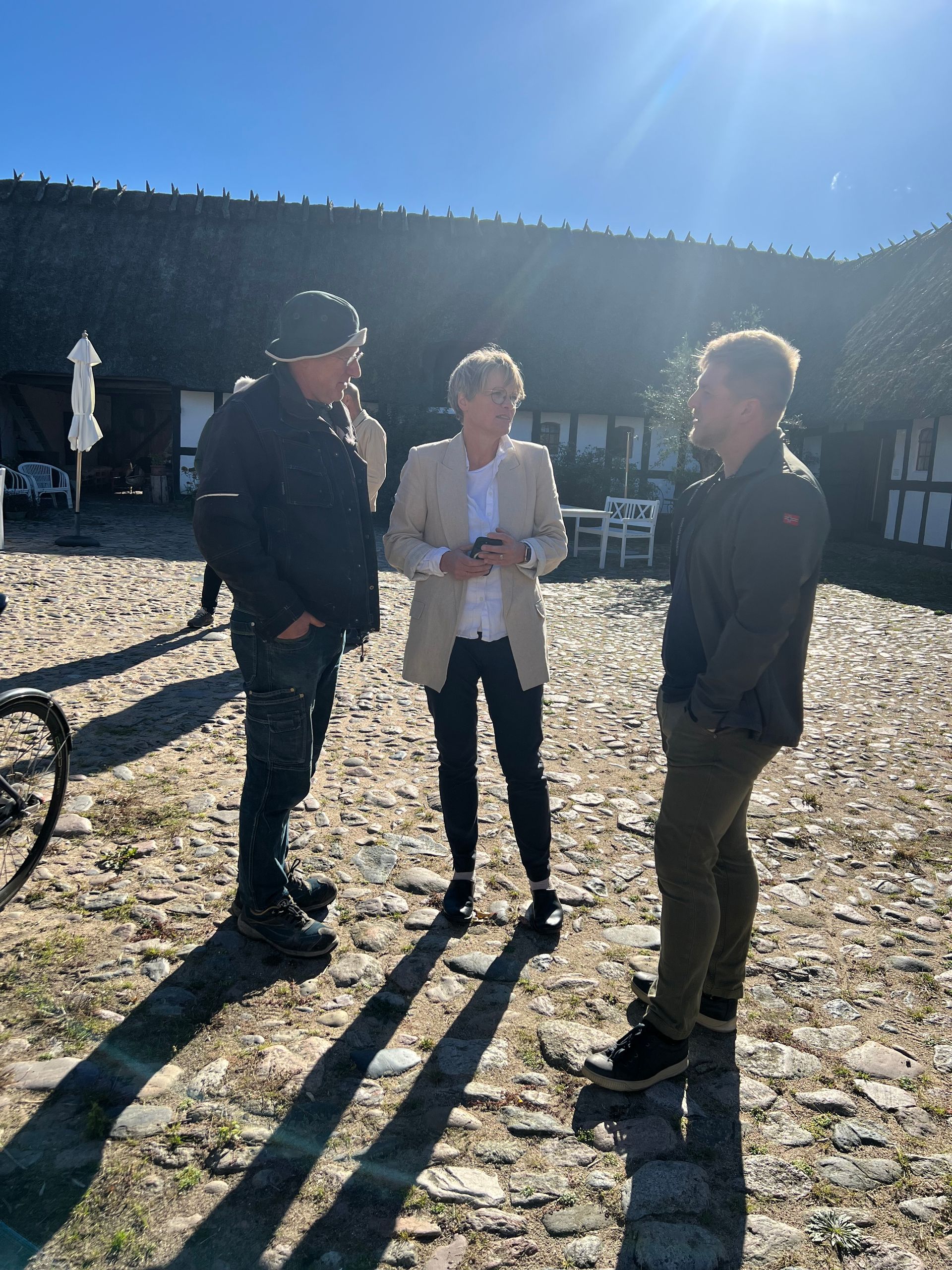 A group of people are standing on a cobblestone street talking to each other.