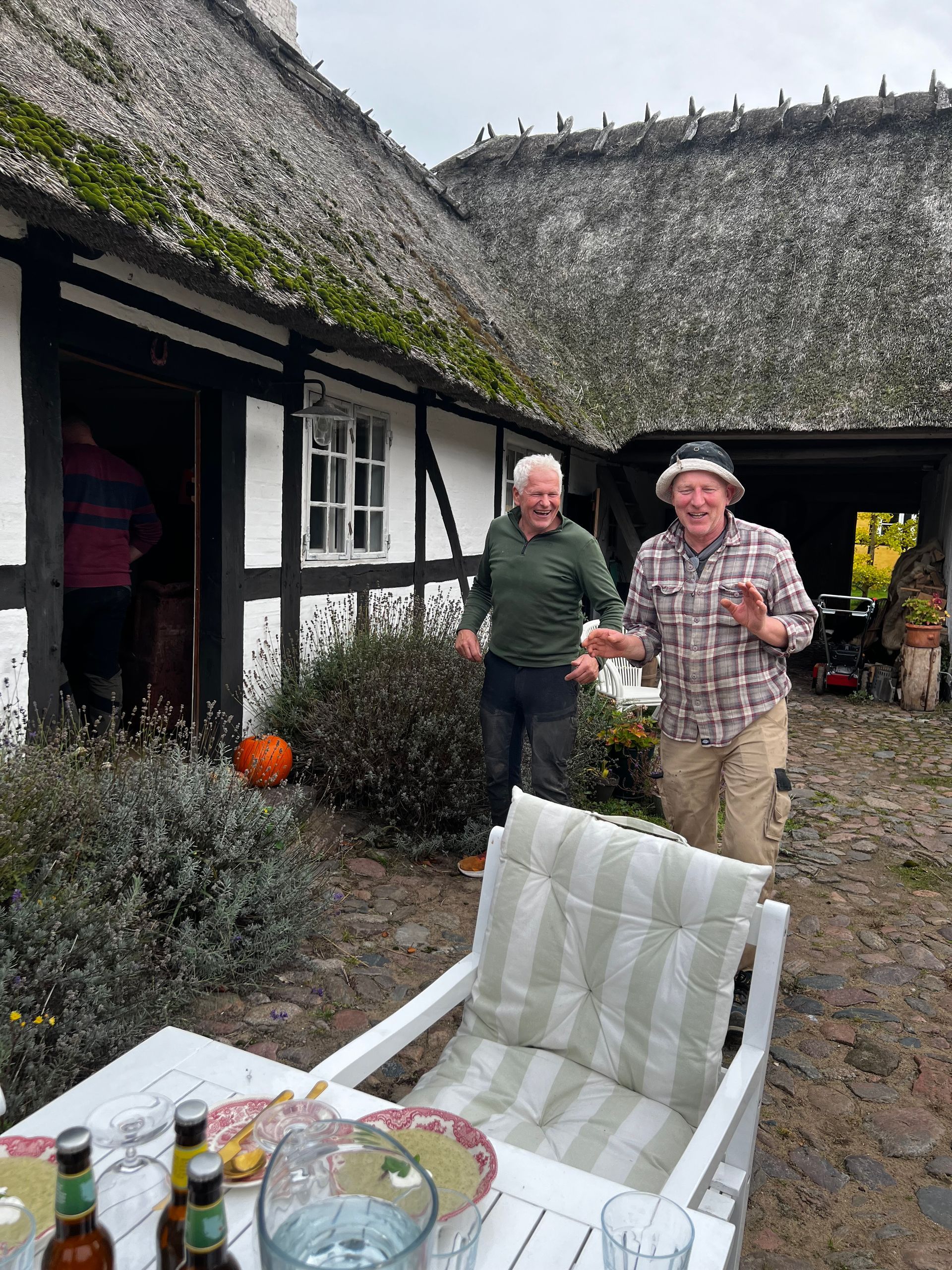 Two men are standing in front of a thatched roof house.
