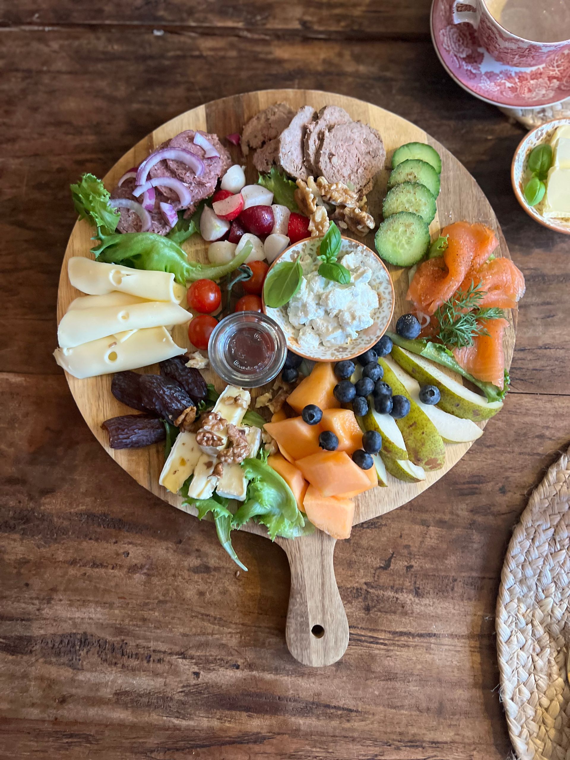 A wooden cutting board filled with a variety of food on a wooden table.
