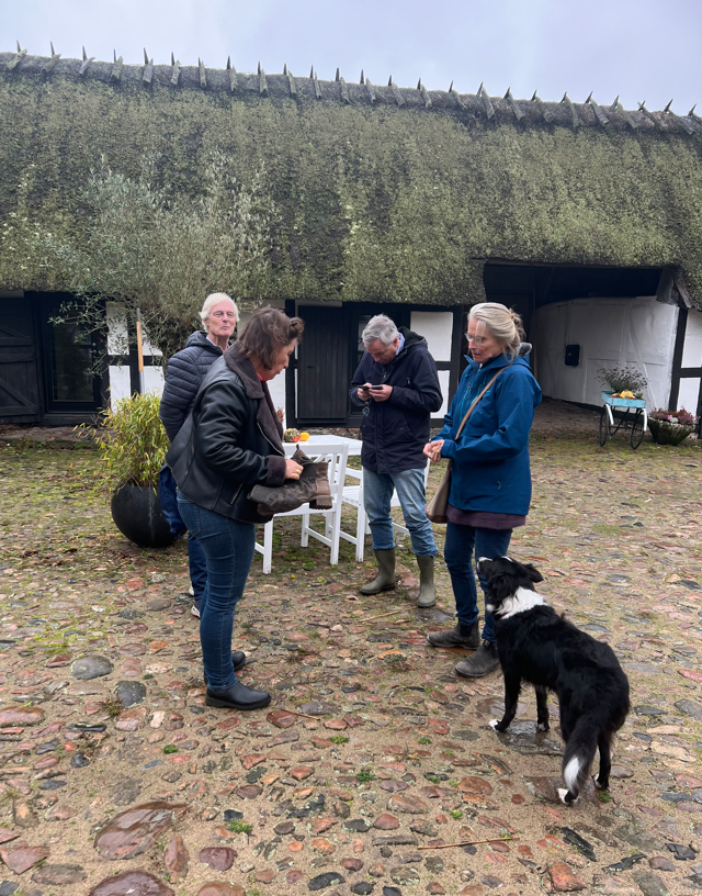 A group of people and a dog are standing in front of a thatched roof house.