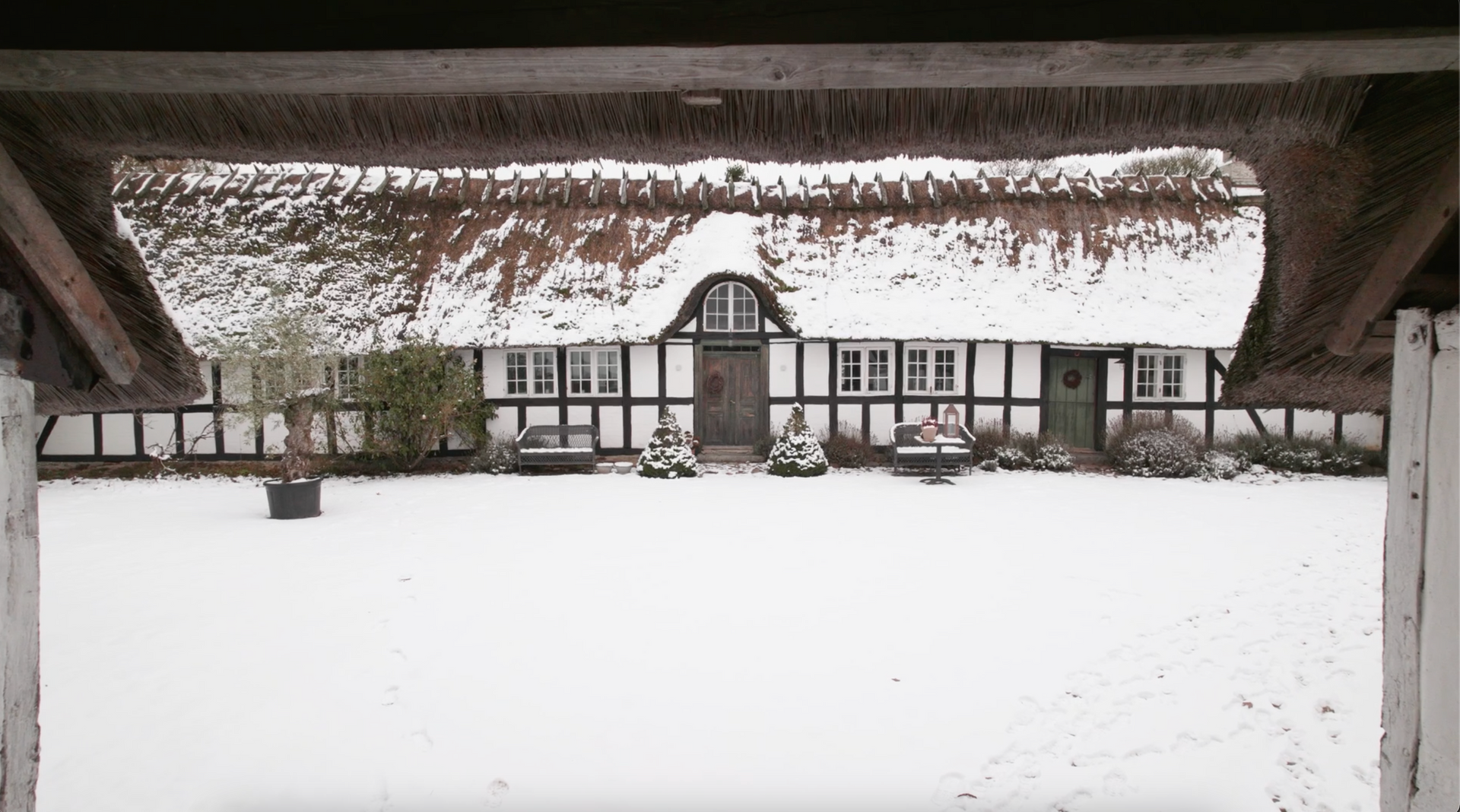 A house with a thatched roof is covered in snow.