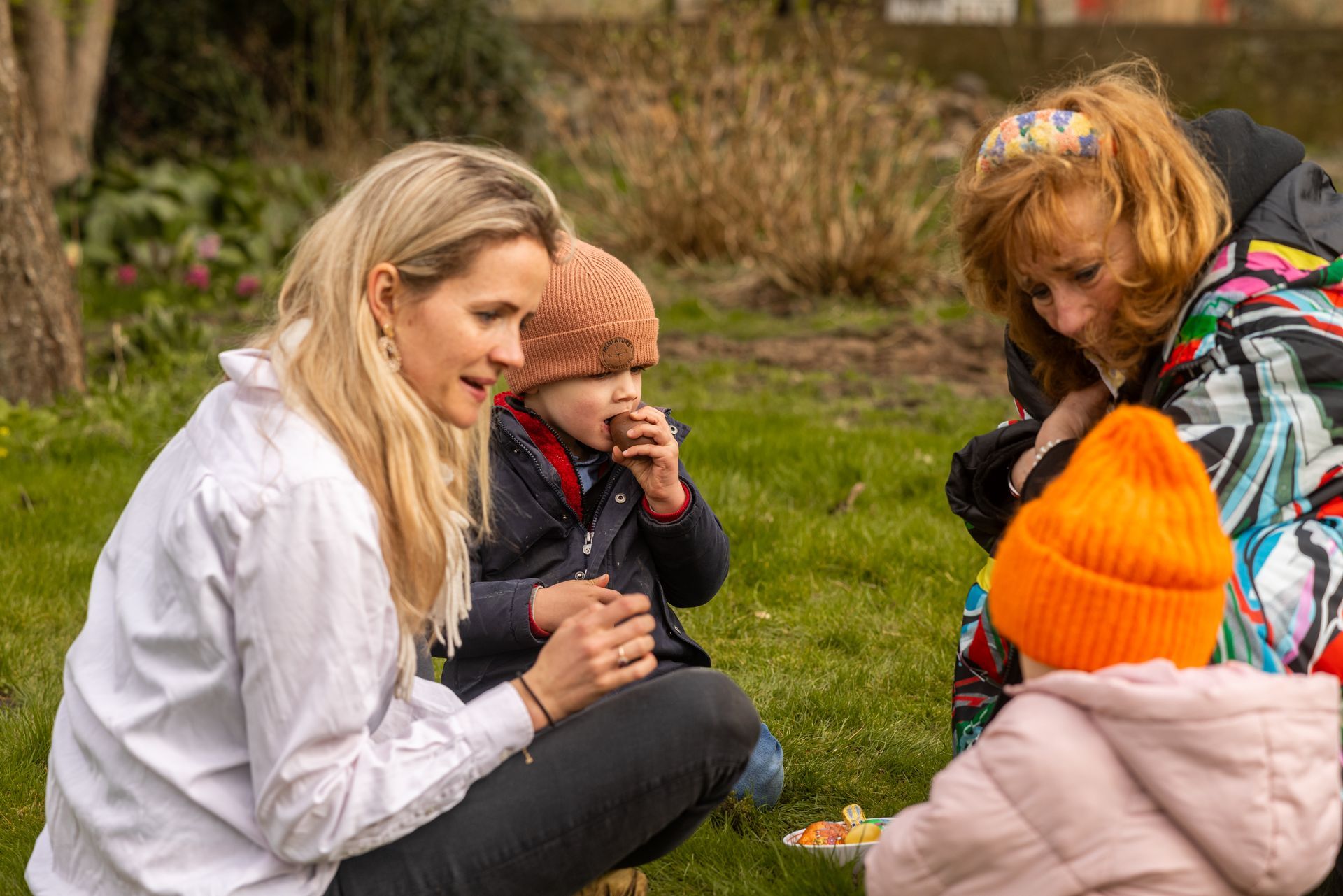 A woman is kneeling down next to two children in the grass.