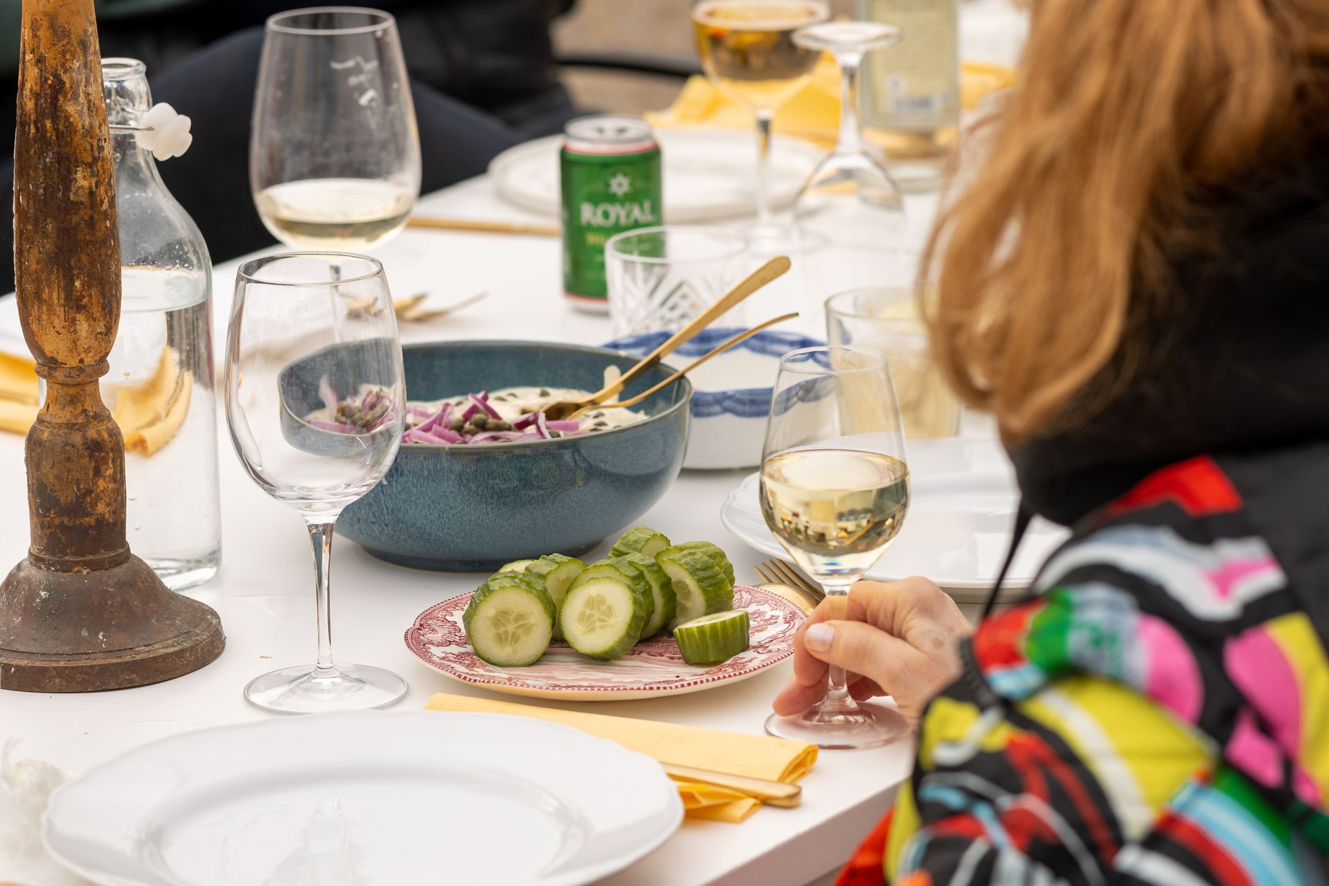 A woman is sitting at a table with plates of food and wine glasses.
