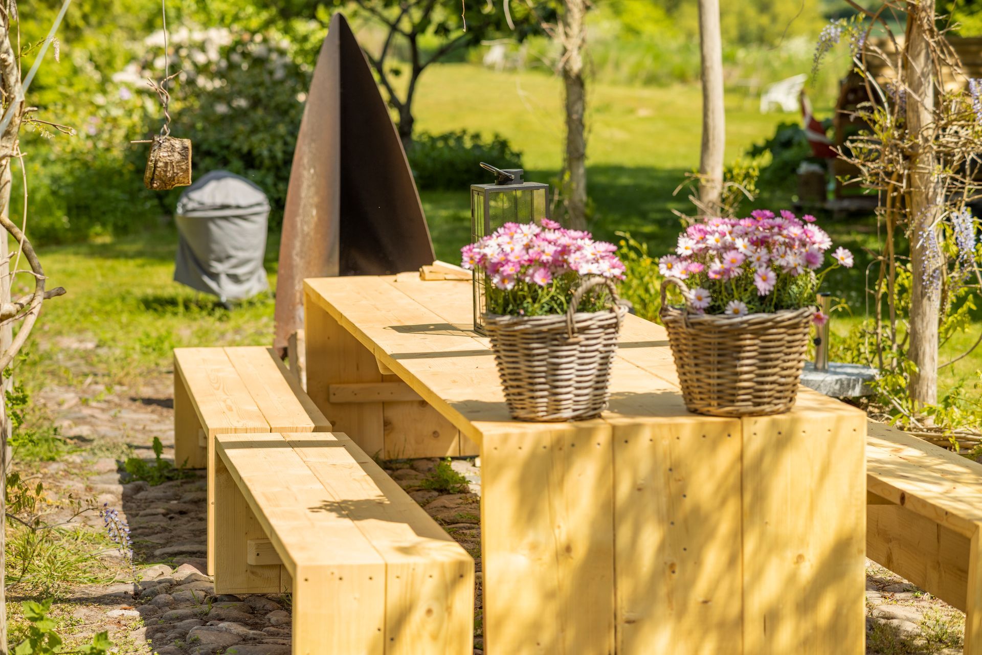 A wooden picnic table with two baskets of flowers on it.