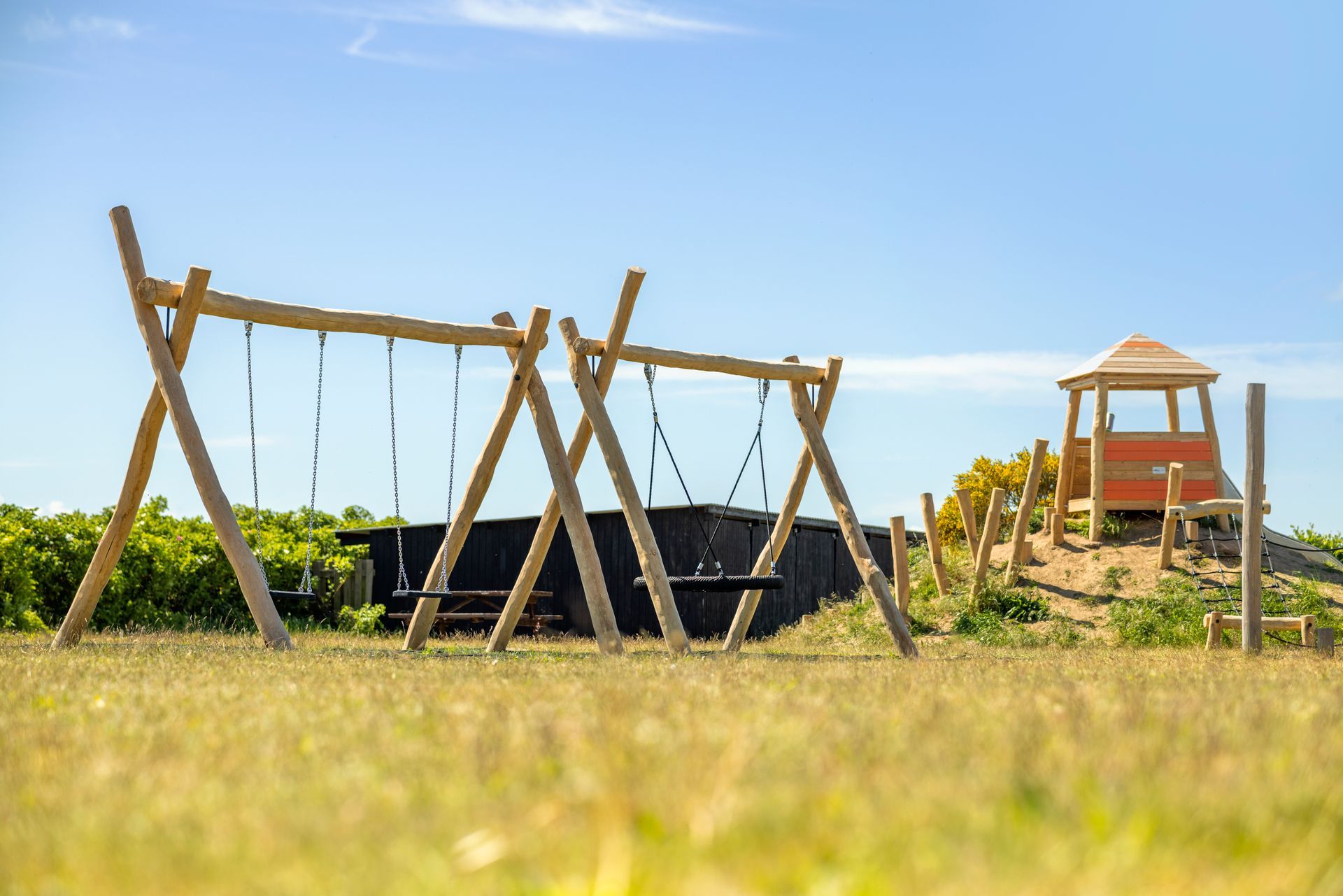 A wooden swing set is sitting in the middle of a field.