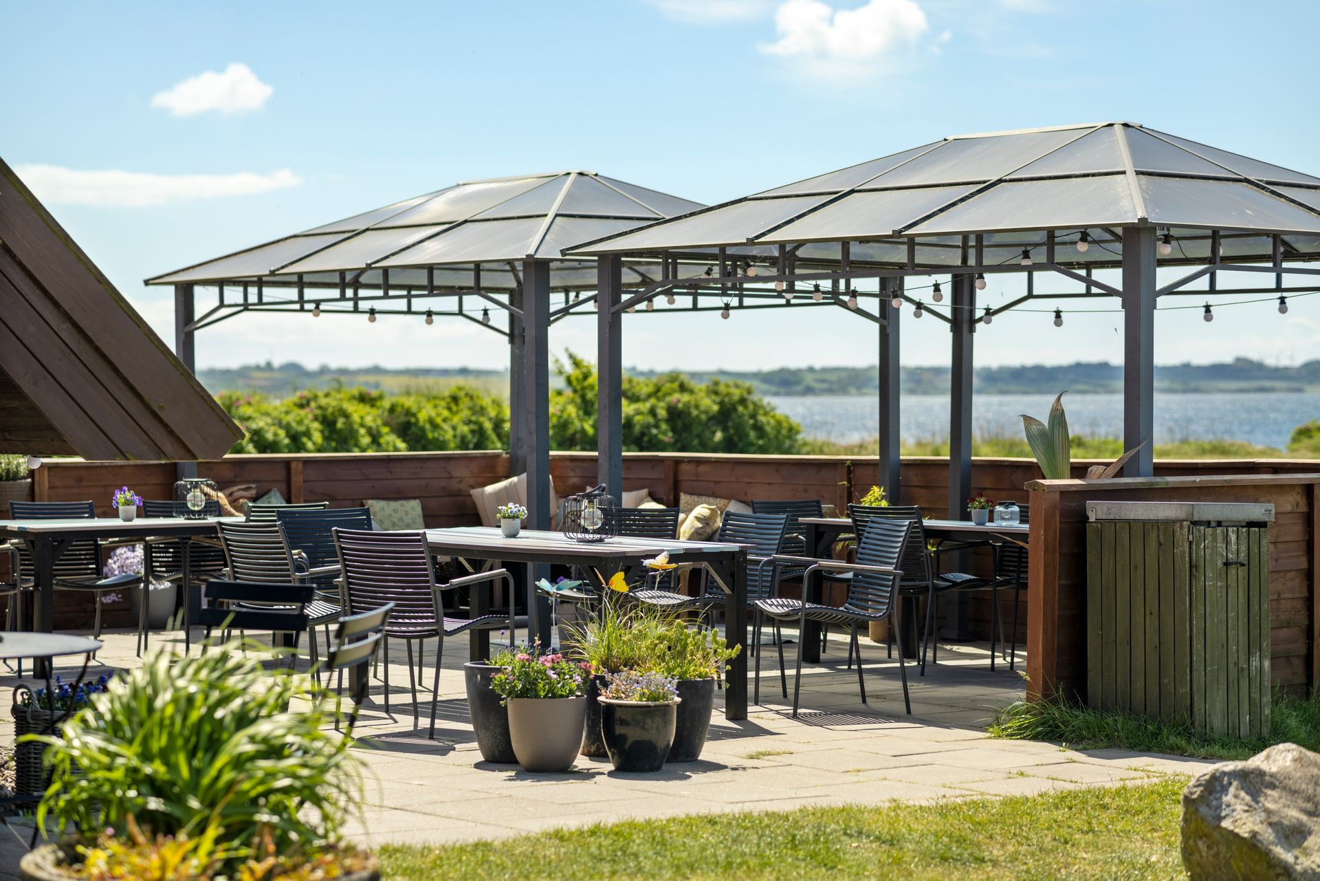 A patio with tables and chairs under umbrellas overlooking a body of water.