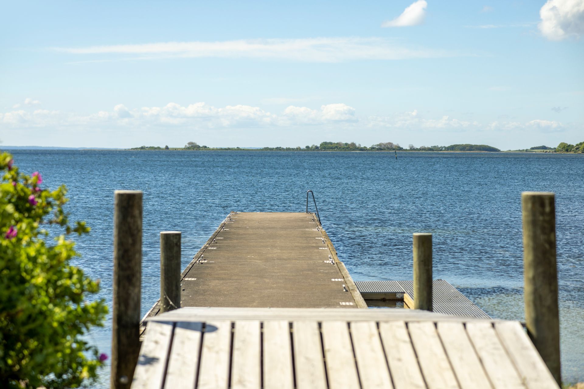 Sun‑lit wooden jetty stretching out into calm blue waters under a clear sky, inviting guests to relax by the sea.