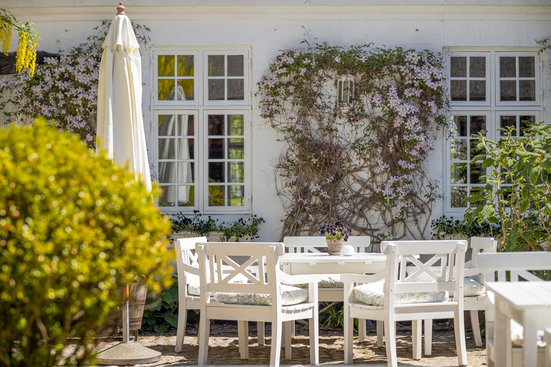 A patio with a table and chairs and an umbrella in front of a white house.