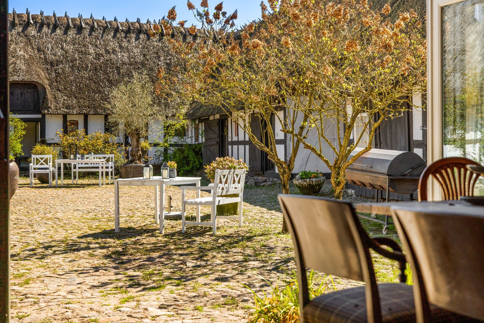 A patio with tables and chairs in front of a house with a thatched roof.