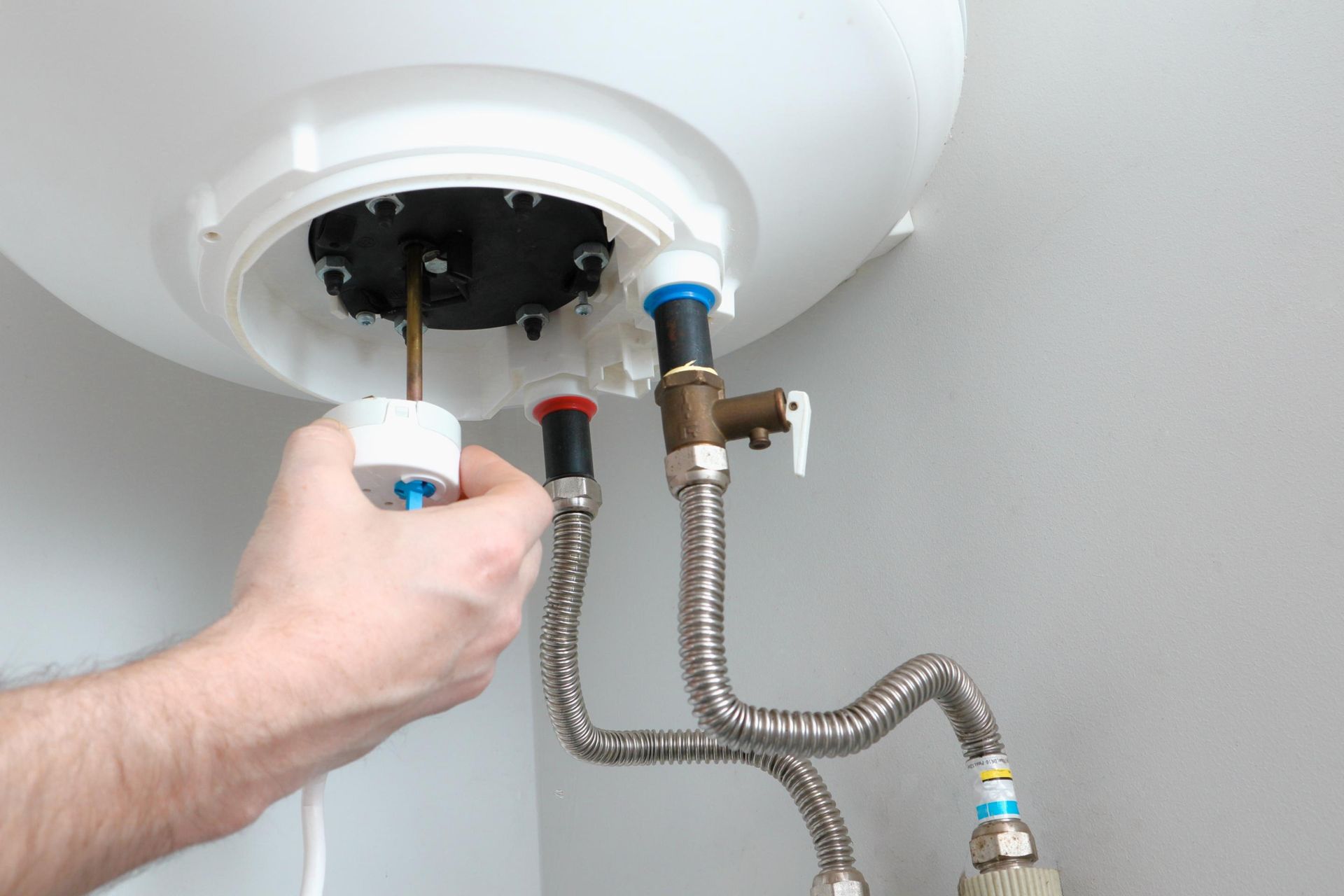 Person installing or repairing a water heater, with plumbing visible.