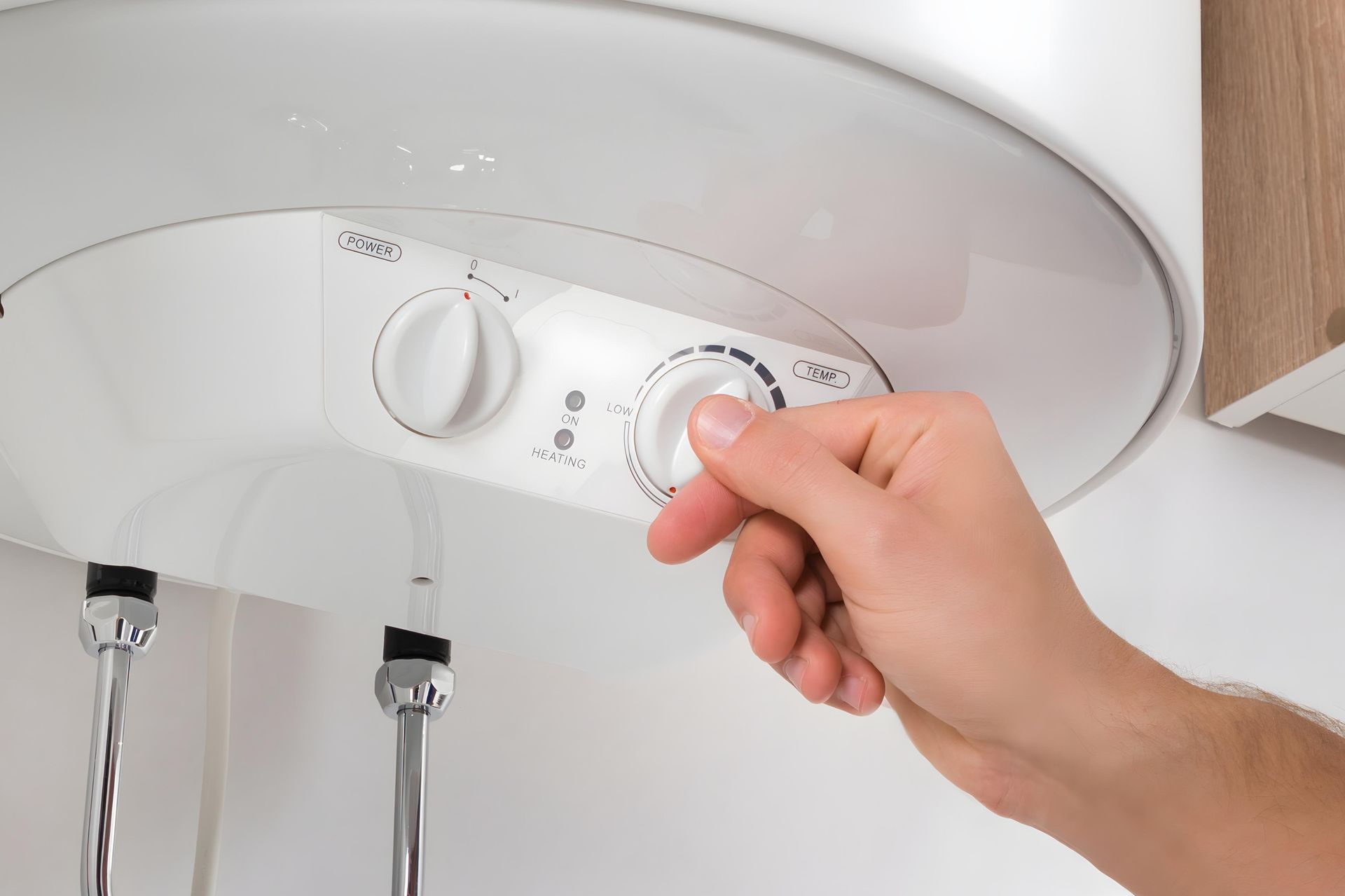 Hand turning a knob on a white water heater, likely adjusting the temperature setting.