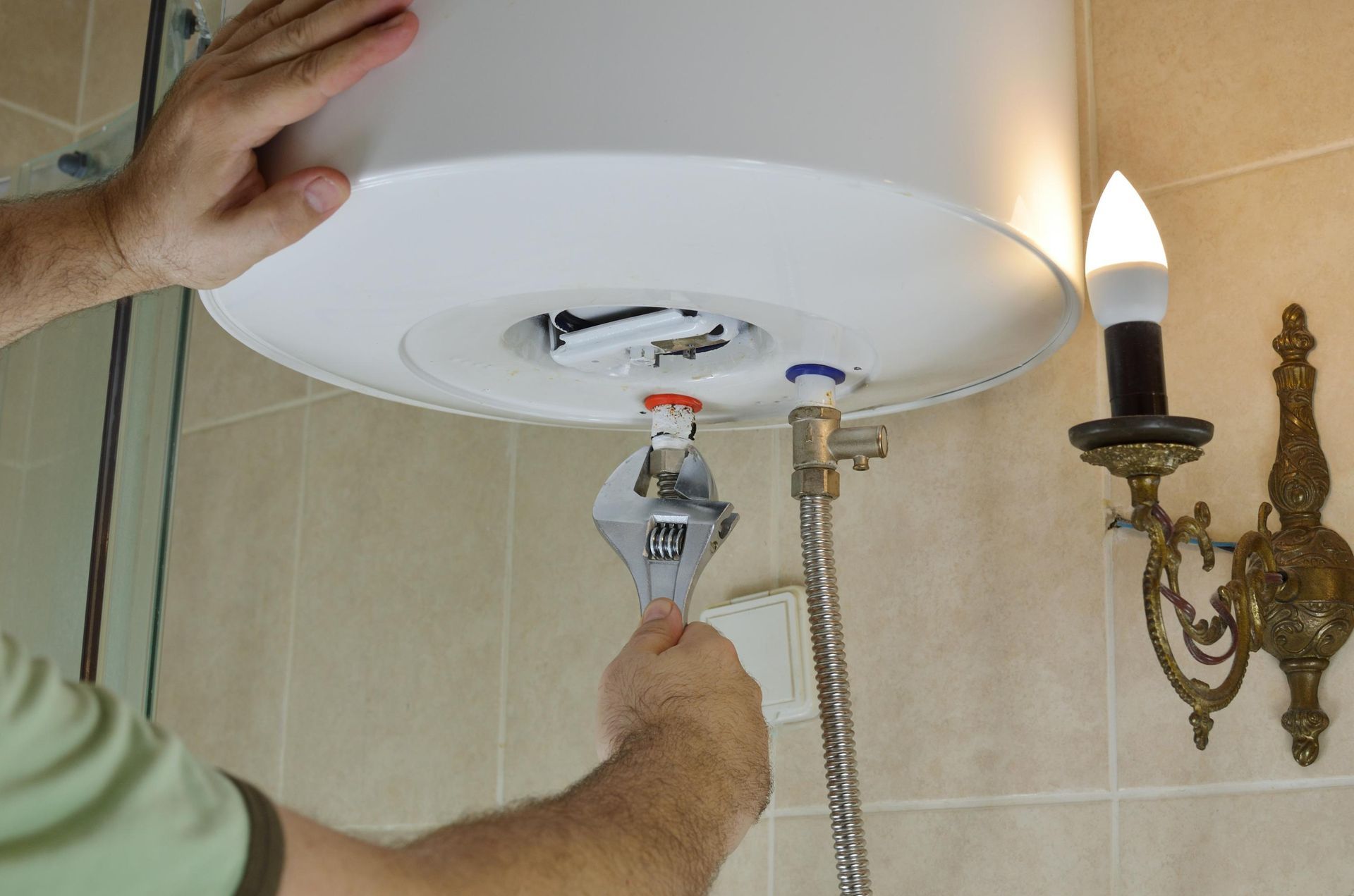 Person using a wrench on a water heater in a tiled bathroom.