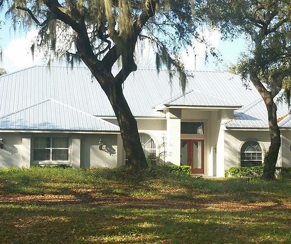 A white house with a metal roof is surrounded by trees