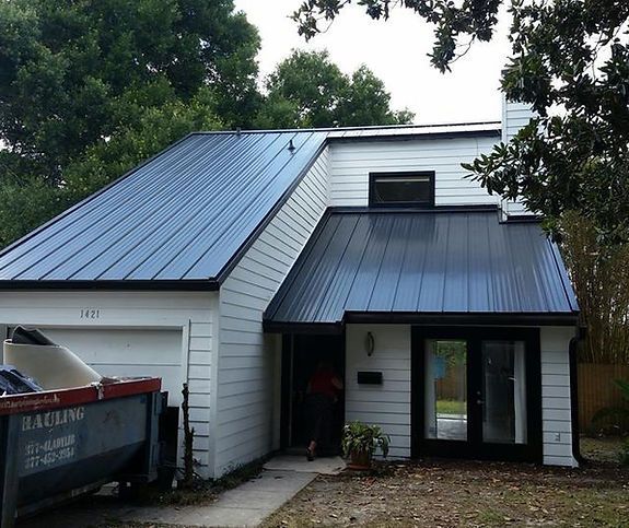 A white house with a black roof and a dumpster in front of it
