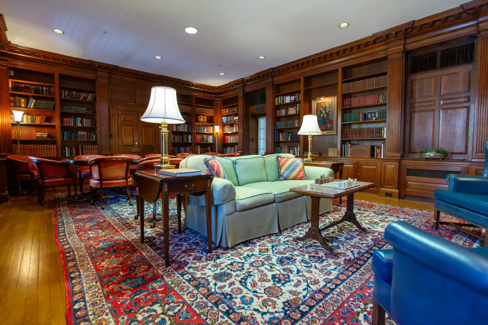 A luxurious library with wooden bookshelves, a sofa, rug, and chairs.